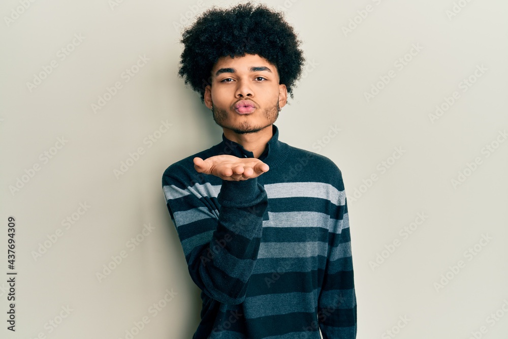 Young african american man with afro hair wearing casual clothes looking at the camera blowing a kiss with hand on air being lovely and sexy. love expression. Young african american man with afro hair wearing casual clothes looking at the camera blowing a kiss with hand on air being lovely and sexy. love expression.