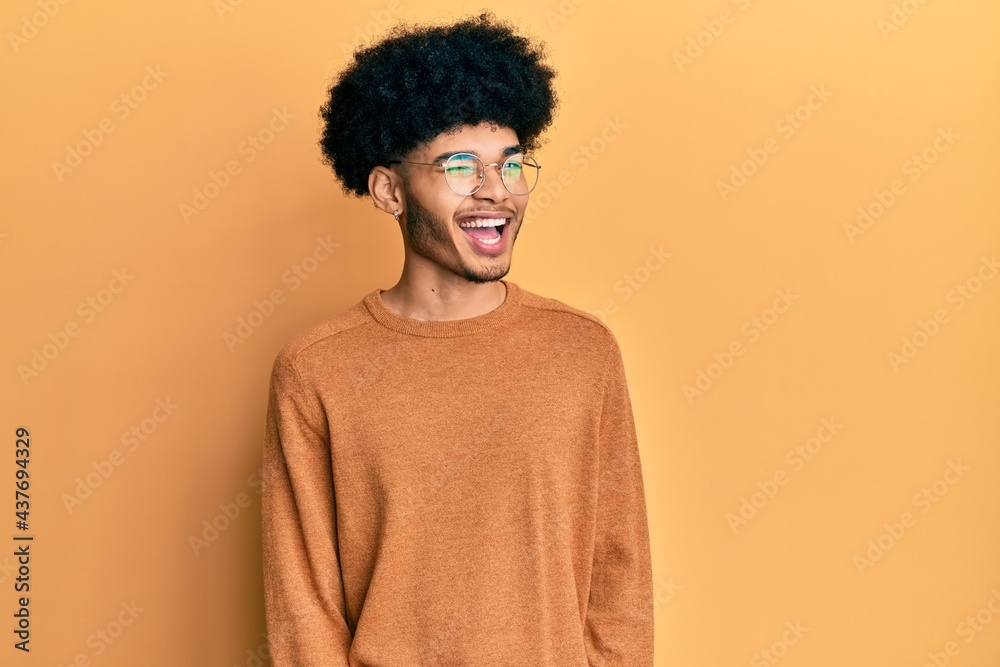 Young african american man with afro hair wearing casual winter sweater winking looking at the camera with sexy expression, cheerful and happy face. Young african american man with afro hair wearing casual winter sweater winking looking at the camera with sexy expression, cheerful and happy face.