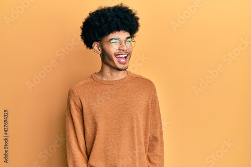 Young african american man with afro hair wearing casual winter sweater winking looking at the camera with sexy expression, cheerful and happy face.