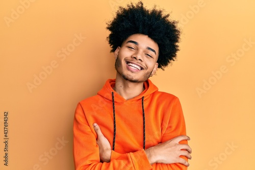 Young african american man with afro hair wearing casual sweatshirt happy face smiling with crossed arms looking at the camera. positive person.