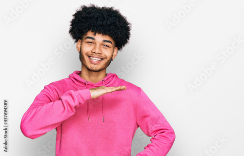 Young african american man with afro hair wearing casual pink sweatshirt gesturing with hands showing big and large size sign, measure symbol. smiling looking at the camera. measuring concept.