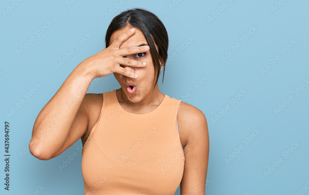 Young brunette woman wearing casual clothes peeking in shock covering face and eyes with hand, looking through fingers with embarrassed expression. Young brunette woman wearing casual clothes peeking in shock covering face and eyes with hand, looking through fingers with embarrassed expression.