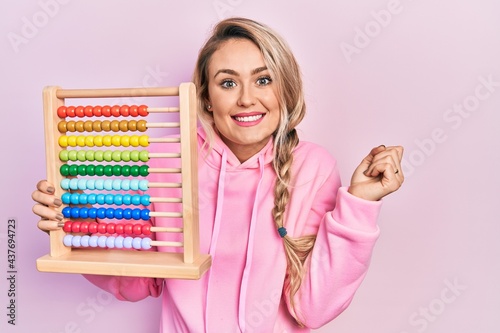 Tablou pe pânză Beautiful young blonde woman holding traditional abacus screaming proud, celebra