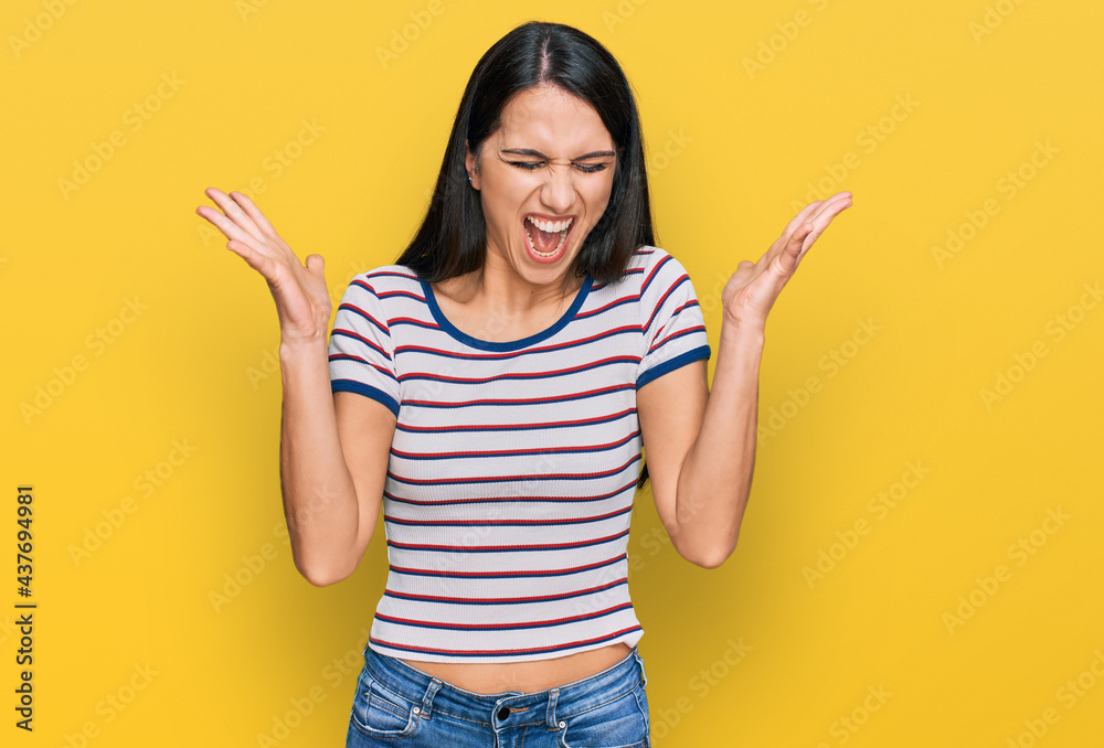 Young hispanic girl wearing casual striped t shirt celebrating mad and crazy for success with arms raised and closed eyes screaming excited. winner concept Young hispanic girl wearing casual striped t shirt celebrating mad and crazy for success with arms raised and closed eyes screaming excited. winner concept
