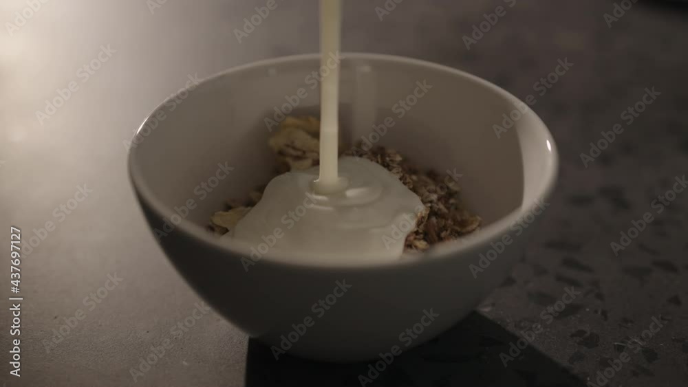 Slow motion pour yogurt on granola in white bowl on concrete countertop Slow motion pour yogurt on granola in white bowl on concrete countertop