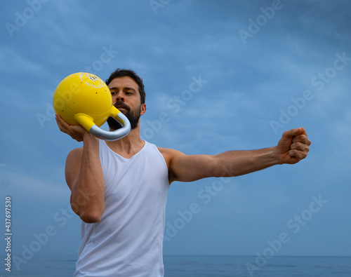 Male athlete exercising at the beach with kettle bells