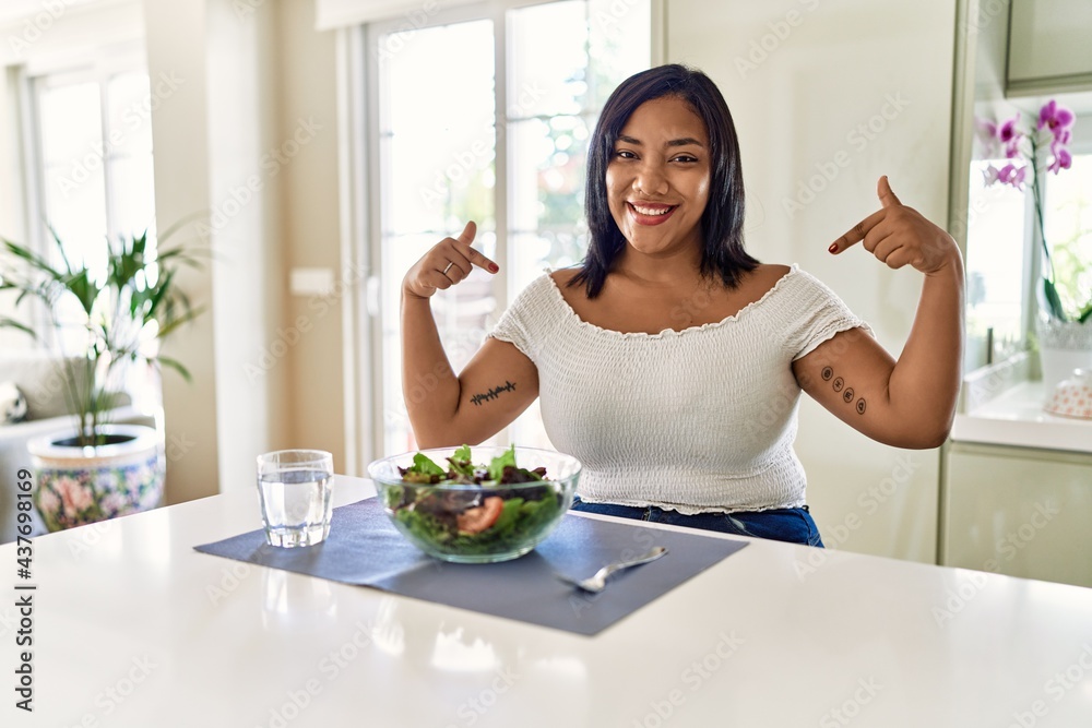 Young hispanic woman eating healthy salad at home looking confident with smile on face, pointing oneself with fingers proud and happy. Young hispanic woman eating healthy salad at home looking confident with smile on face, pointing oneself with fingers proud and happy.