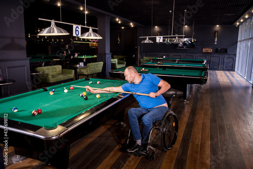 Adult man with disability in a wheelchair play billiards in the club