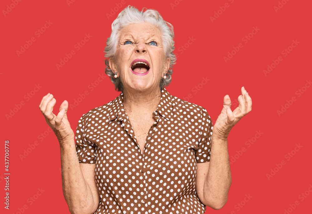 Senior grey-haired woman wearing casual clothes crazy and mad shouting and yelling with aggressive expression and arms raised. frustration concept. Senior grey-haired woman wearing casual clothes crazy and mad shouting and yelling with aggressive expression and arms raised. frustration concept.