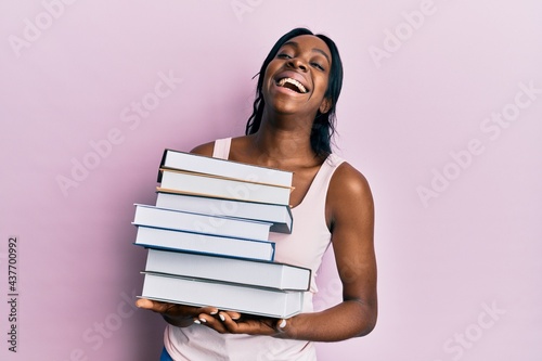 Young african american woman holding books smiling and laughing hard out loud because funny crazy joke.