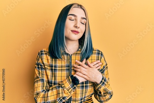 Young modern girl wearing casual yellow shirt smiling with hands on chest, eyes closed with grateful gesture on face. health concept. © Krakenimages.com