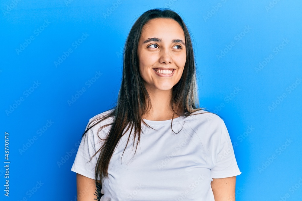Young hispanic woman wearing casual white t shirt looking away to side with smile on face, natural expression. laughing confident. Young hispanic woman wearing casual white t shirt looking away to side with smile on face, natural expression. laughing confident.