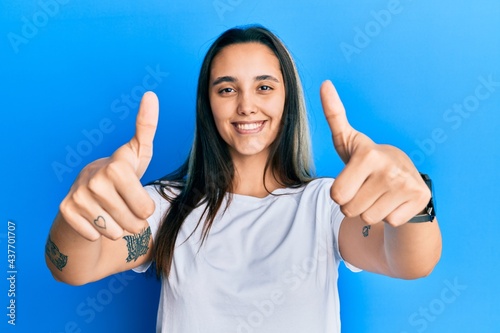 Young hispanic woman wearing casual white t shirt approving doing positive gesture with hand, thumbs up smiling and happy for success. winner gesture. © Krakenimages.com