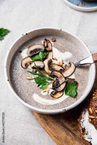 Traditional French mushroom cream soup with sour cream and parsley and rye bun on wooden board on natural linen background .