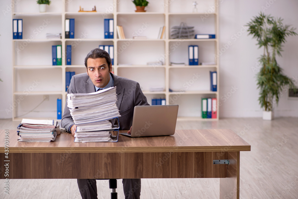Young male employee unhappy with excessive work in the office Young male employee unhappy with excessive work in the office