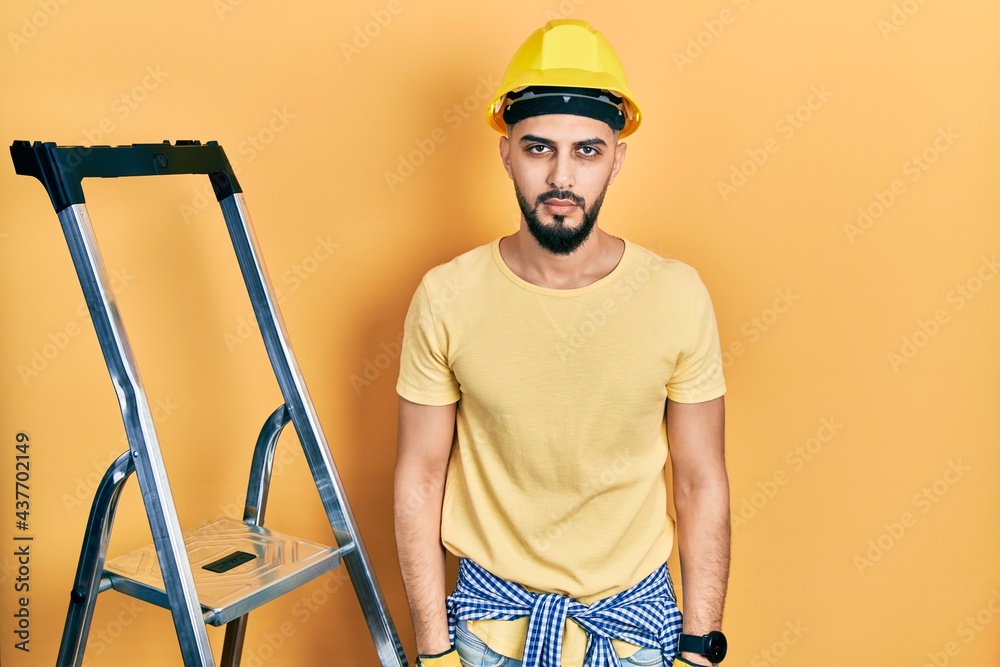 Handsome man with beard by construction stairs wearing hardhat relaxed with serious expression on face. simple and natural looking at the camera. Handsome man with beard by construction stairs wearing hardhat relaxed with serious expression on face. simple and natural looking at the camera.