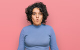 Young hispanic woman with curly hair wearing casual clothes making fish face with lips, crazy and comical gesture. funny expression.