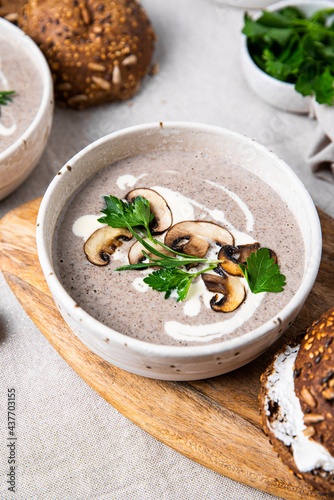Traditional French mushroom cream soup with sour cream and parsley and rye bun on wooden board on natural linen background .