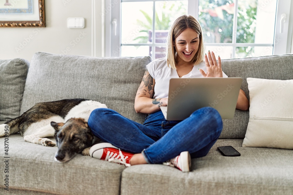 Young caucasian girl sitting on the sofa with dog having video call using laptop at home. Young caucasian girl sitting on the sofa with dog having video call using laptop at home.