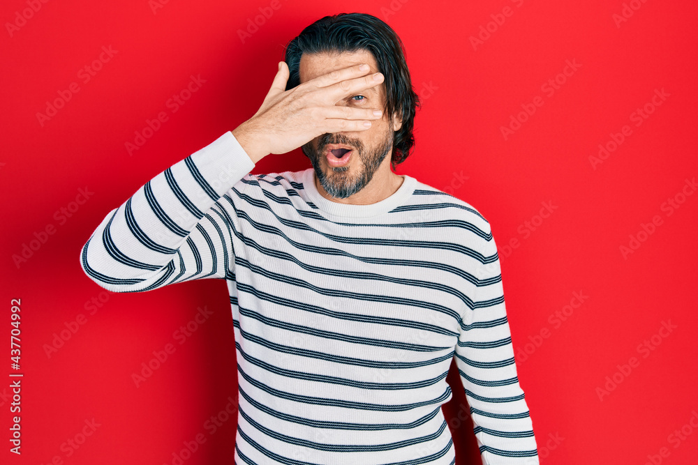 Middle age caucasian man wearing casual clothes peeking in shock covering face and eyes with hand, looking through fingers afraid