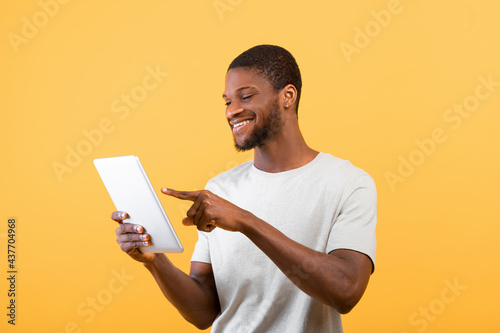 African american male blogger using digital tablet, surfing in internet, isolated on yellow background, studio shot