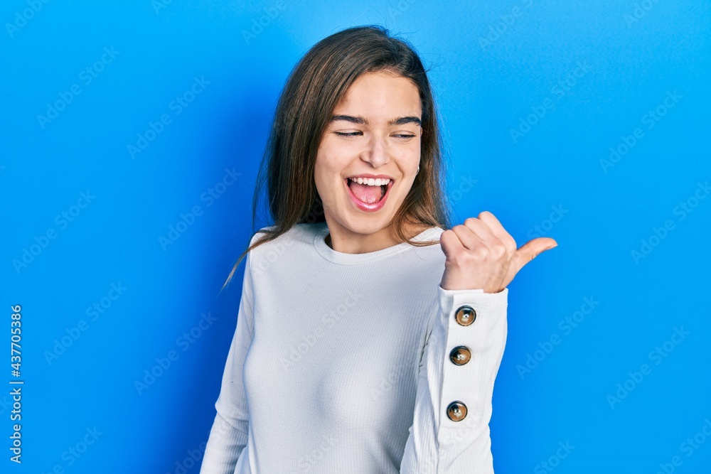 Young caucasian girl wearing casual clothes pointing thumb up to the side smiling happy with open mouth Young caucasian girl wearing casual clothes pointing thumb up to the side smiling happy with open mouth