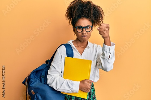 Beautiful african american woman with afro hair wearing school bag and holding books annoyed and frustrated shouting with anger, yelling crazy with anger and hand raised