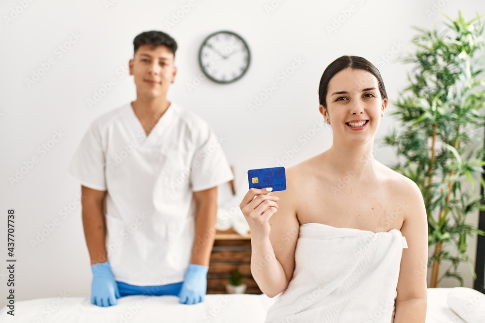 Obraz premium Woman smiling happy waiting to recive massage holding credit card at beauty center.