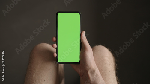 Man using phone with green screen while sitting with naked legs