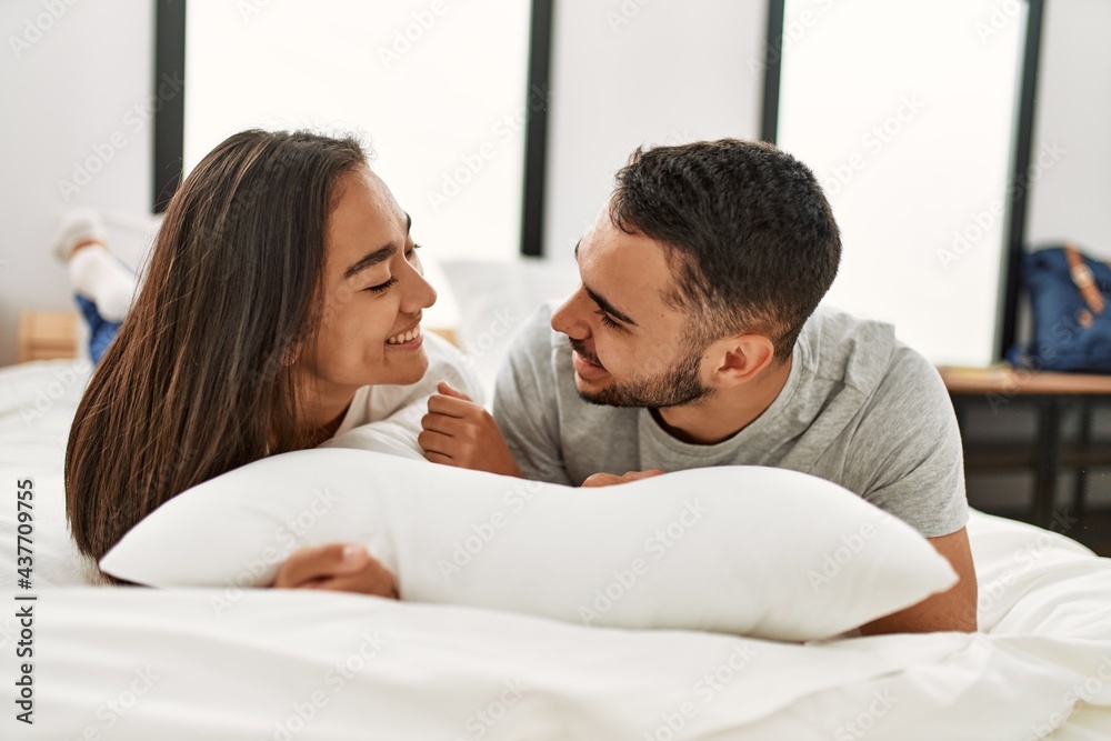 Fototapeta premium Young latin couple smiling happy hugging on the bed at home.