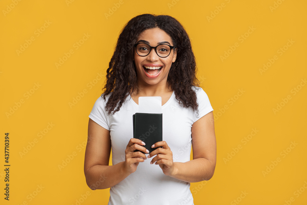 Cheap flights. Overjoyed black lady holding passport and tickets, standing over yellow background Cheap flights. Overjoyed black lady holding passport and tickets, standing over yellow background