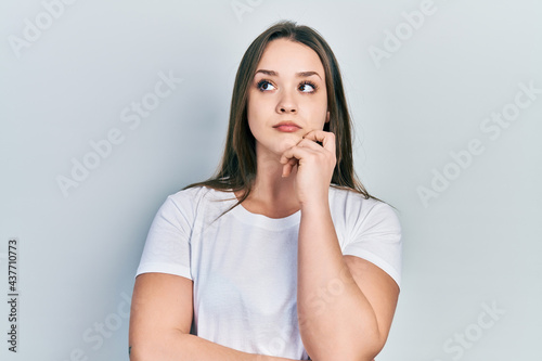 Young hispanic girl wearing casual white t shirt thinking concentrated about doubt with finger on chin and looking up wondering