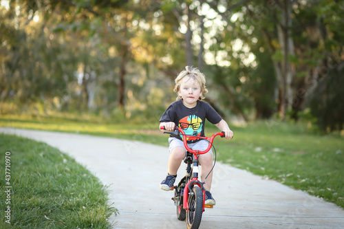 Fototapeta Naklejka Na Ścianę i Meble -  Little boy riding bike along walking track in pretty Australian bush setting at sunset