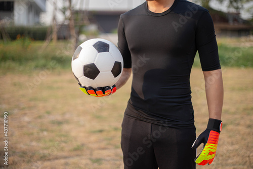 Sports and recreation concept a male teenage goalkeeper wearing black outfit and a pair of colorful gloves holding a soccer © Pichsakul