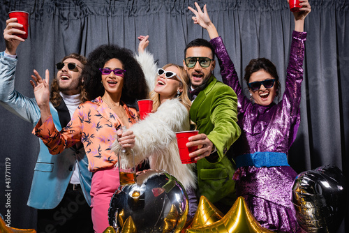 smiling interracial friends in sunglasses having party on grey background.
