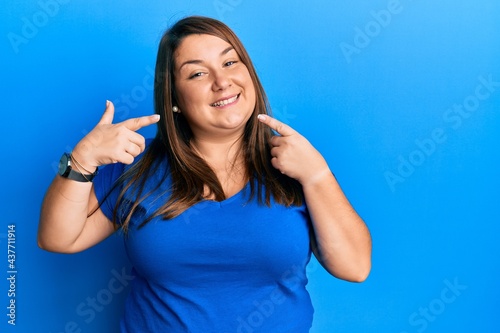 Beautiful brunette plus size woman wearing casual blue t shirt smiling cheerful showing and pointing with fingers teeth and mouth. dental health concept.