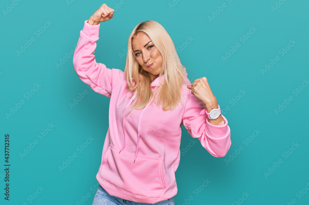 Fototapeta premium Young blonde woman wearing casual sweatshirt showing arms muscles smiling proud. fitness concept.
