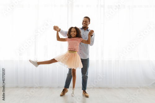 Black father and daughter dancing by window, full length shot