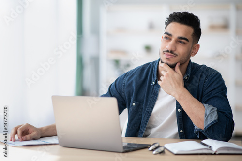 Dreamy young man sitting at office, looking at copy space