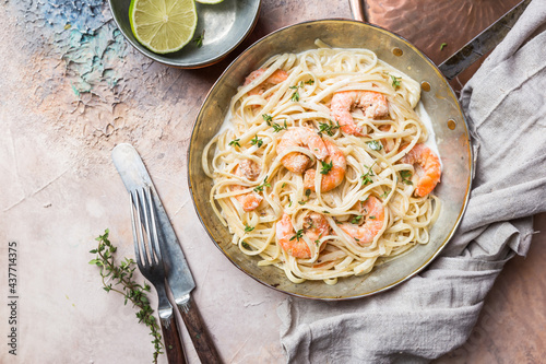 Italian pasta fettuccine in a creamy sauce with shrimp on a copper pan, top view