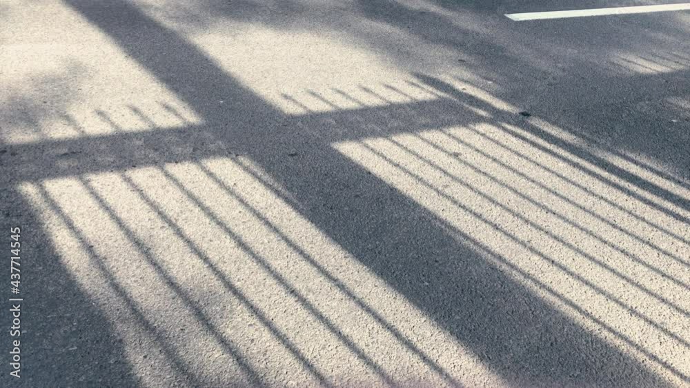 Soft Shadows lattice fence on the asphalt at sunny summer morning. Sunlight through the fence on the asphalt surface. Geometric silhouette Overlay effect for video production.