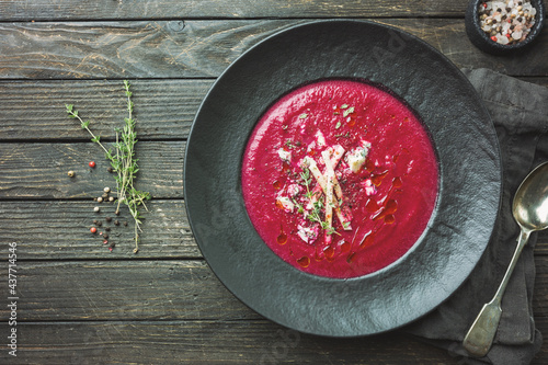 Cold Beetroot mashed soup with cream, apple, cheese and thyme in a dark bowl over wooden background, top view.