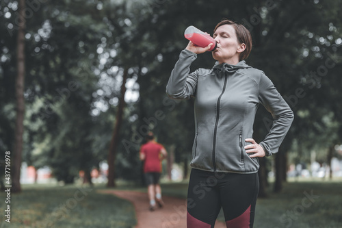 Female jogger drinking refreshing strawberry juice in park