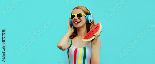 Summer portrait of cheerful happy smiling young woman in headphones listening to music with juicy slice of watermelon on a blue background © rohappy