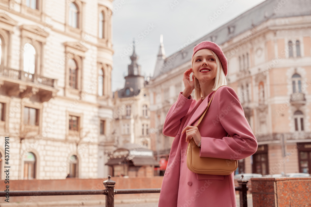 Fototapeta premium Elegant smiling woman wearing stylish pink blazer, beret, with yellow shoulder bag, posing in street of European city. Copy, empty space for text