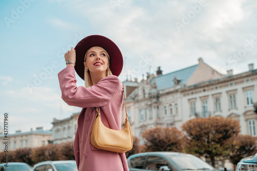 Happy smiling woman wearing elegant pink suit blazer,  with yellow shoulder bag, walking in street of European city. Copy, empty space for text
