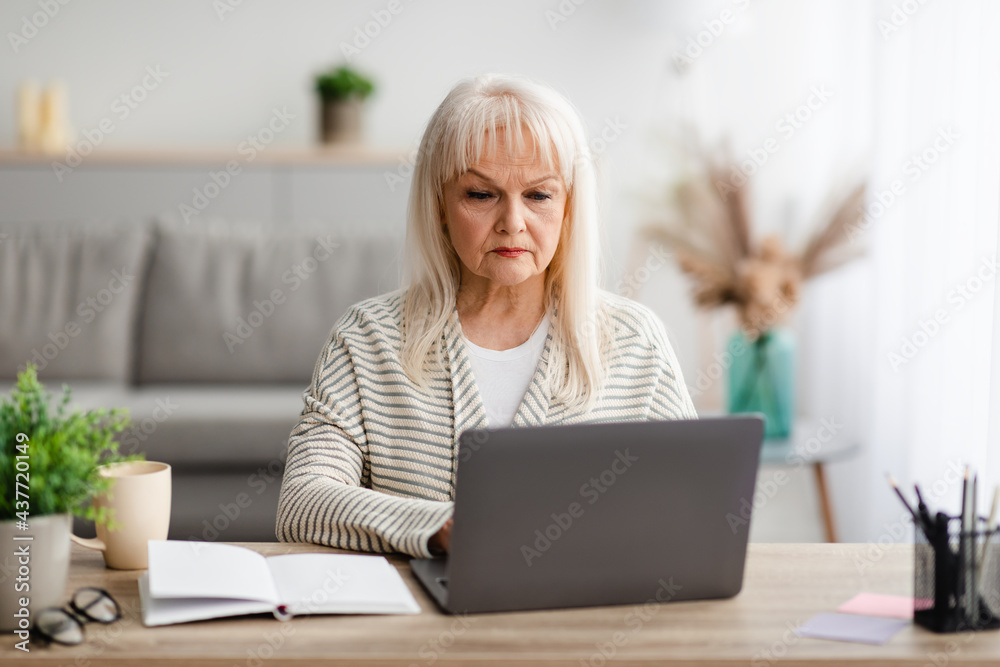 Focused mature woman sitting ot desk and working on computer Focused mature woman sitting ot desk and working on computer