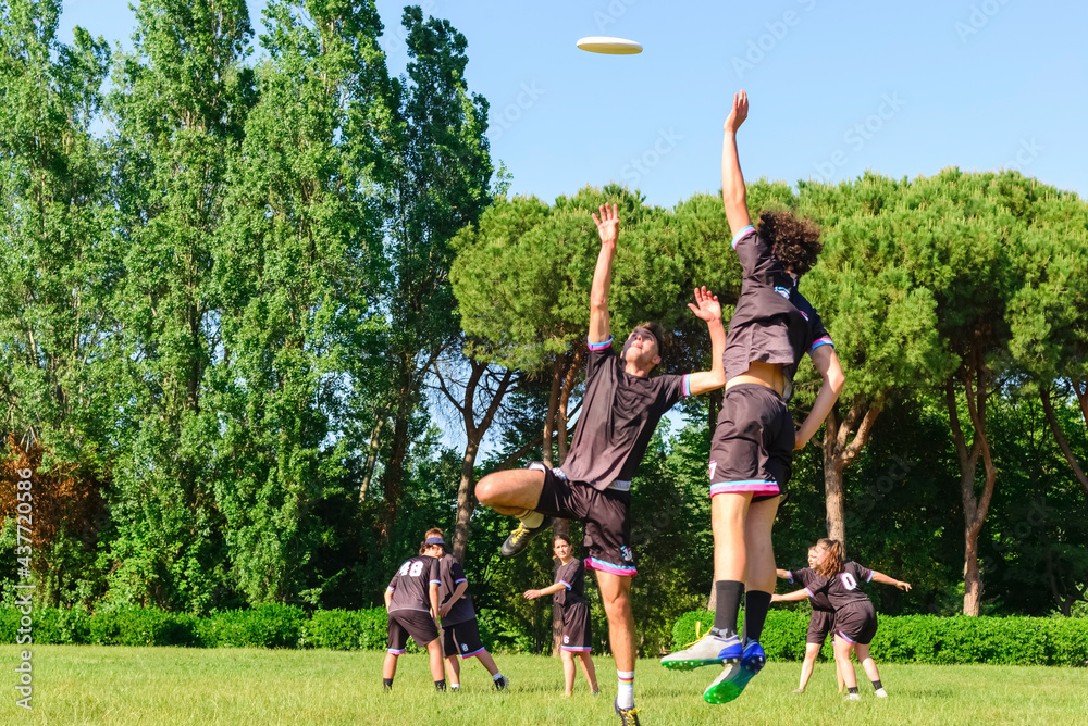 Group of young teenagers people in team wear playing a frisbee game in park  oudoors. jumping