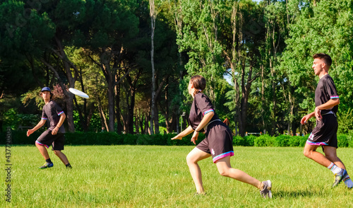 Group of young teenagers people in team wear playing a frisbee game in park oudoors. man tosses a frisbee to a teammate in an ultimate frisbee match. milennials friends outside in a garden having fun photo
