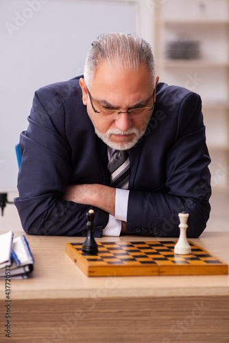 Old male employee playing chess at workplace